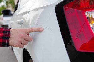 A close-up of a car’s surface with a light scratch being pointed at, showing an area that can be corrected with a cut and polish