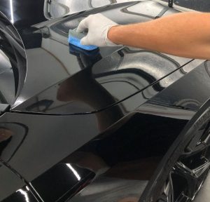  "A gloved hand applying ceramic coating to the black surface of a car, ensuring professional paint protection and a flawless finish."